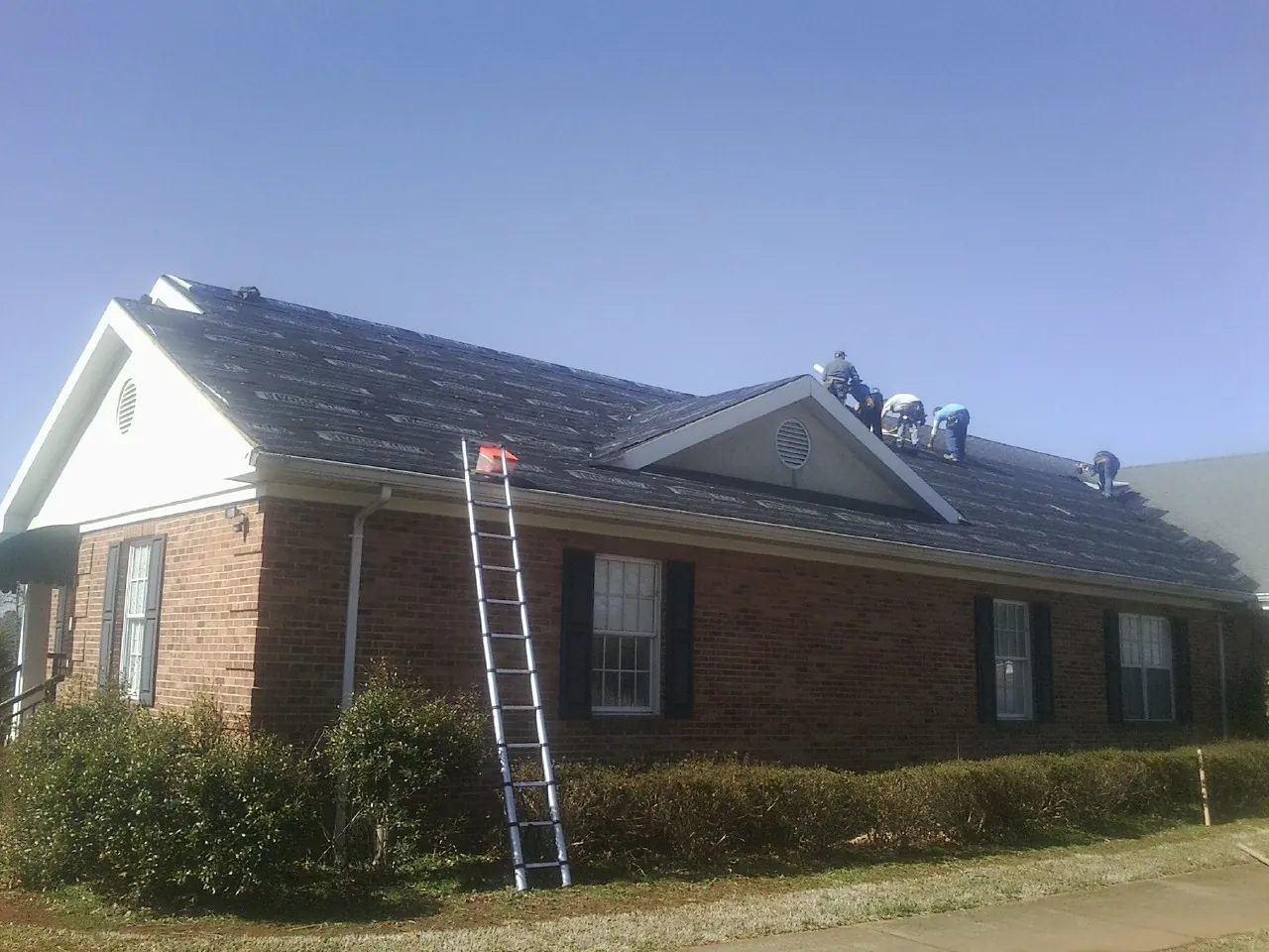 Crew tearing shingles off a brick ranch roof with a ladder set — Emergency Roof Repair work by our crew in Melfa