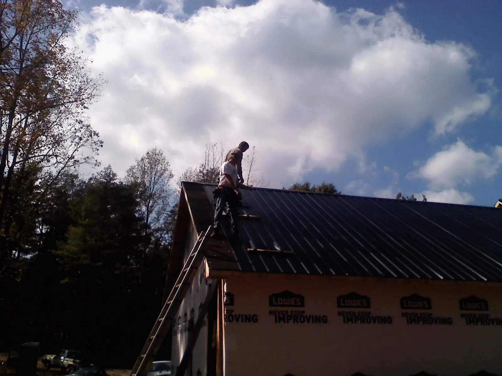 Roofer fastening dark metal panels high against a cloudy sky, from a Roof Inspection job in Melfa